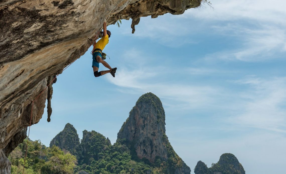 man climbing cliff beside beach