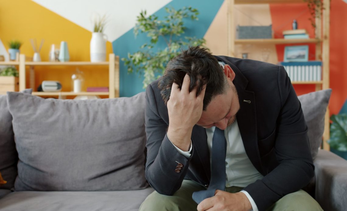 Man in suit sitting on couch with head in hands.