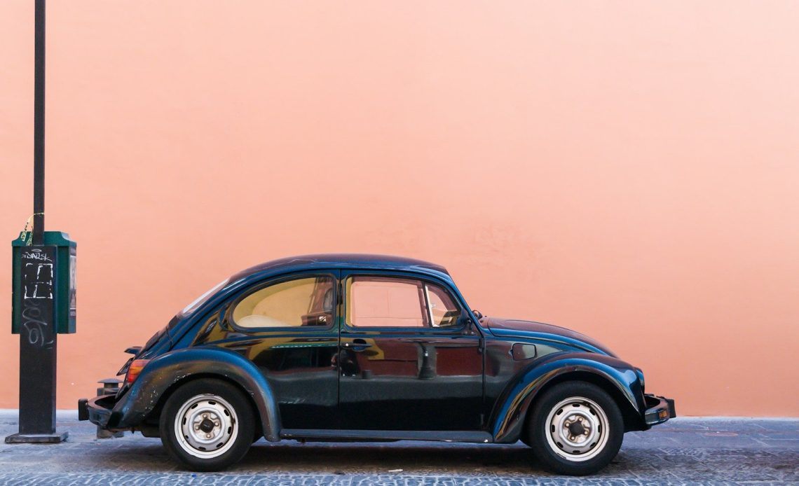 black Volkswagen Beetle beside beige wall