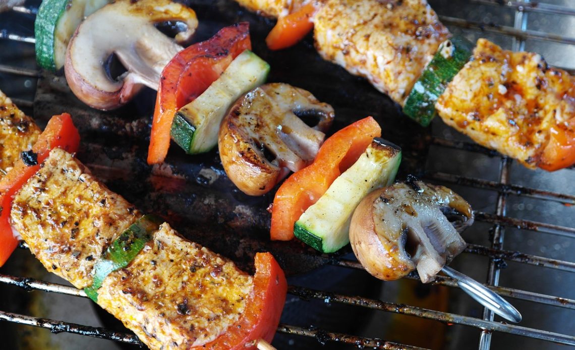 Man staat bij een barbecue en grilt vlees op houtskool