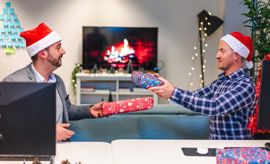 a couple of men wearing santa hats and holding a present