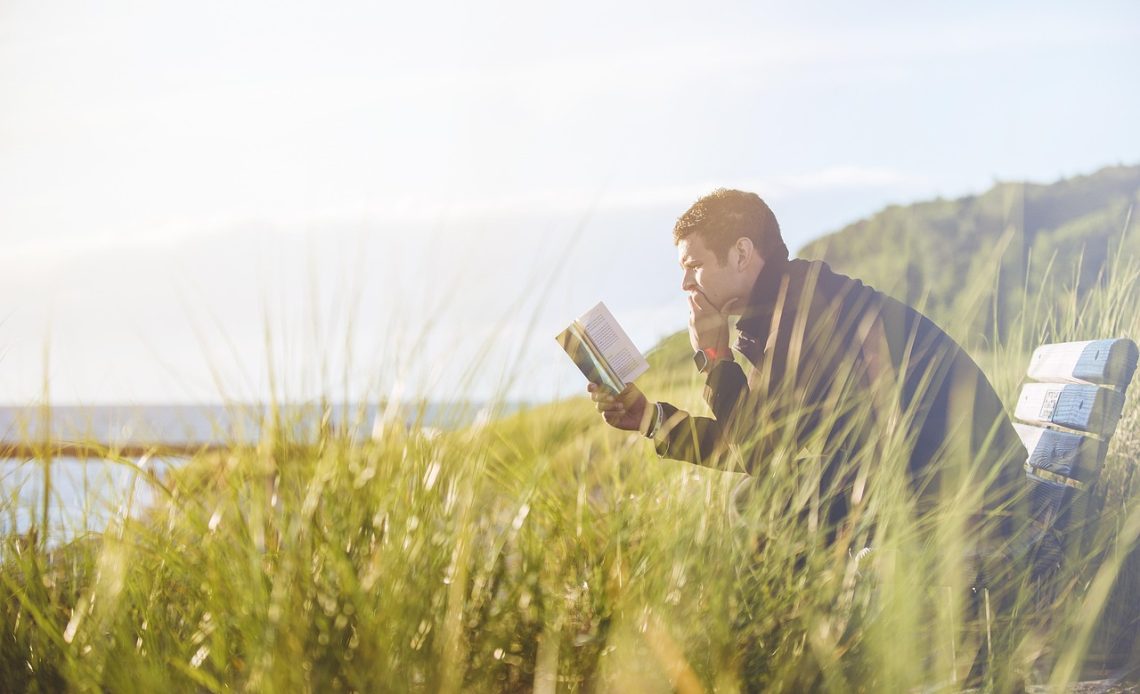 Man die een boek leest buiten, verdiept in gedachten
