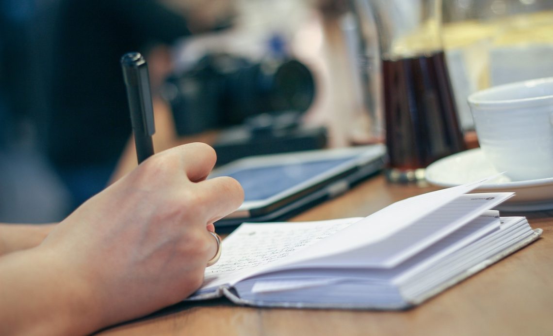 Jonge man schrijft in een notitieboek aan zijn bureau, bezig met zelfreflectie en persoonlijke ontwikkeling